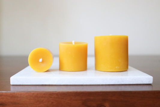 Three beeswax pillar candles on a white marble slab with a neutral background